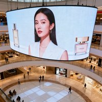 大型购物中心室内中庭，巨大的LED曲面屏悬挂在顶部，播放着品牌广告